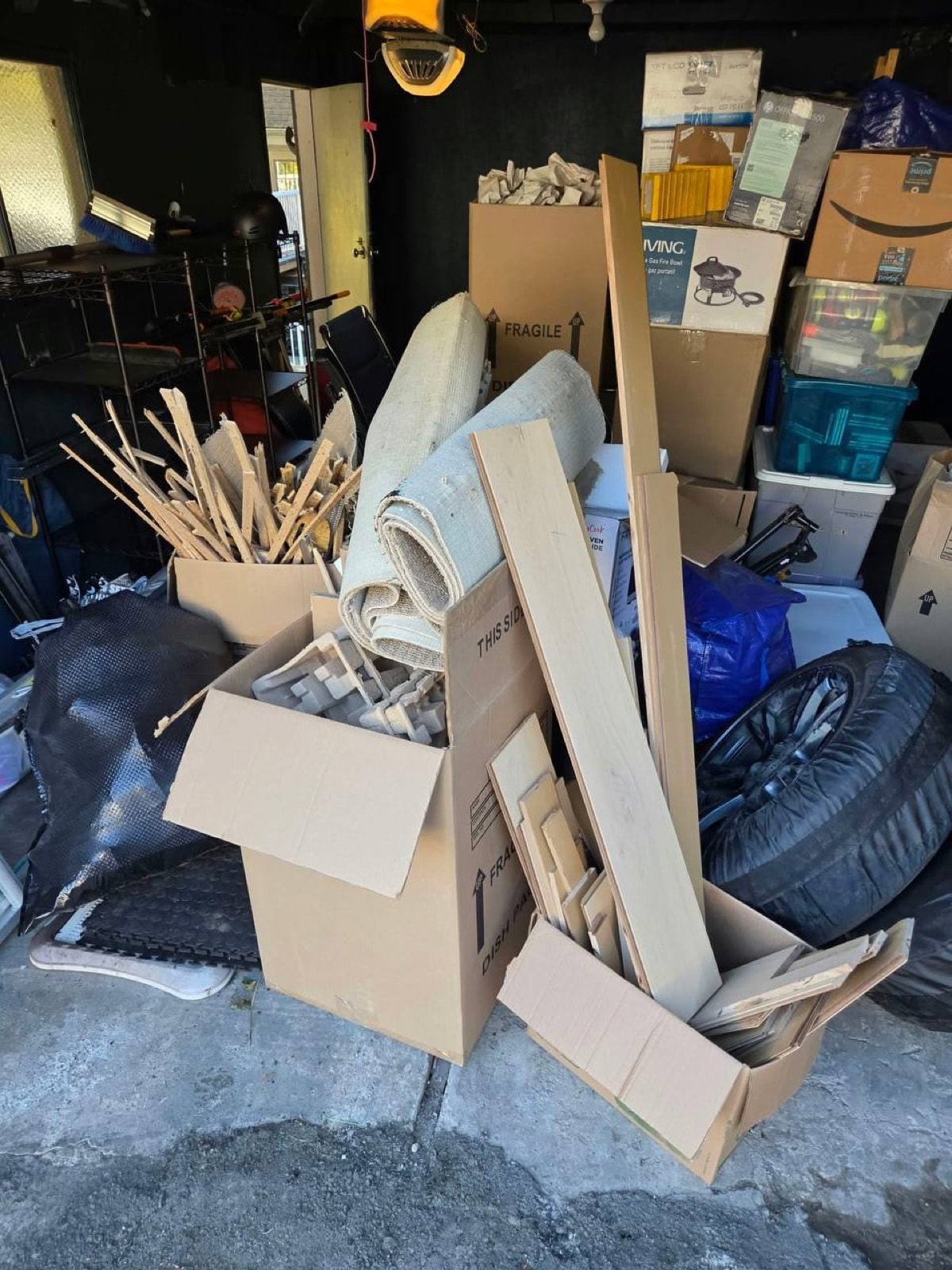 Cluttered garage full of boxes, flooring offcuts and tires before a garage cleanout