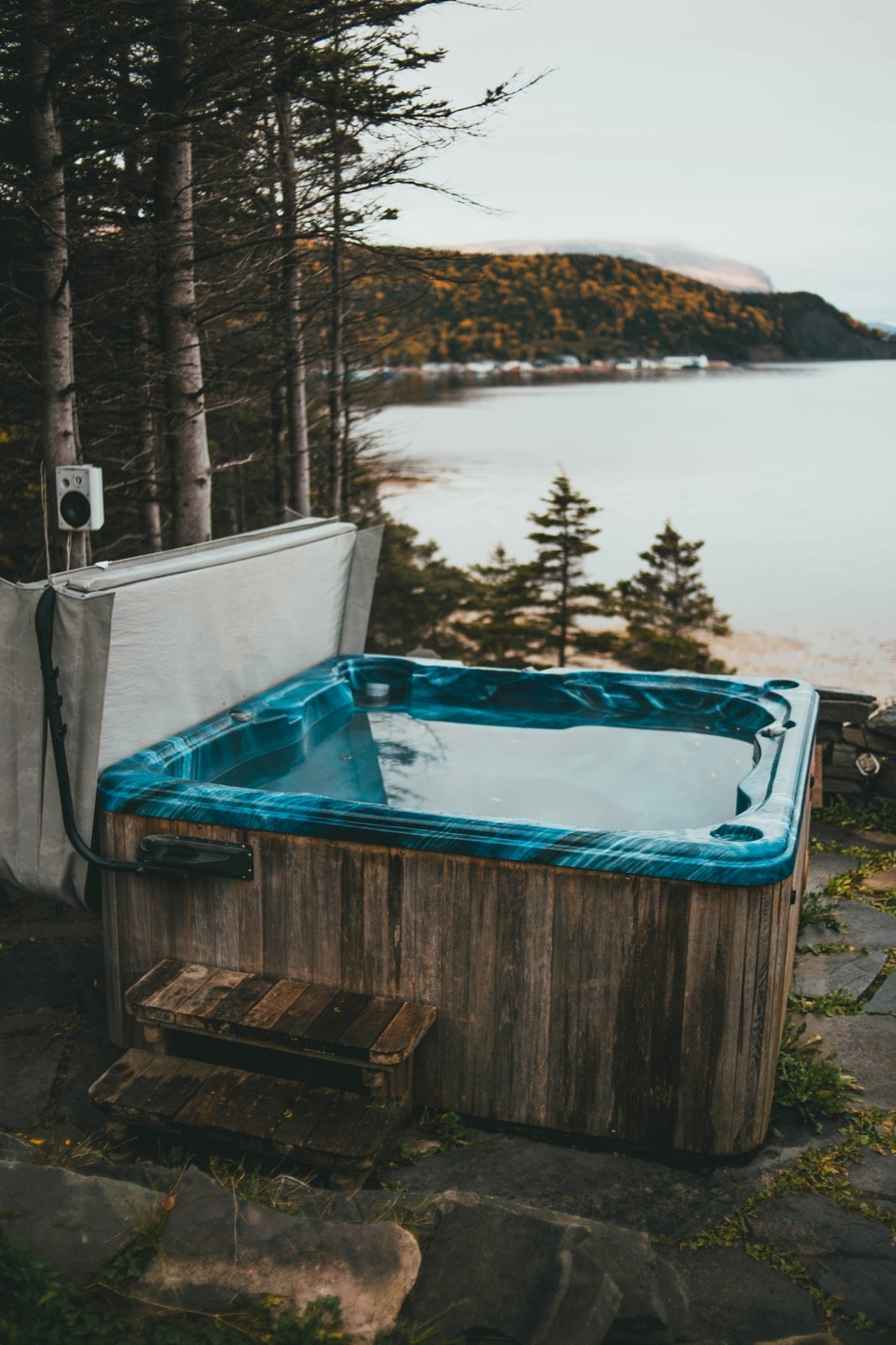 Old wood-sided hot tub with worn cover in a backyard, ready for hot tub removal