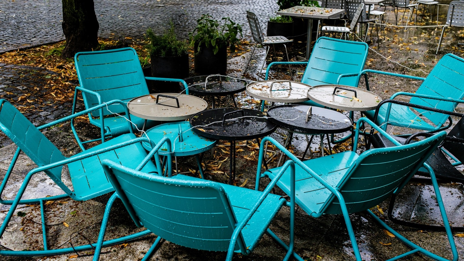 Rain-soaked metal patio chairs and side tables covered in fallen leaves, ready for patio furniture removal