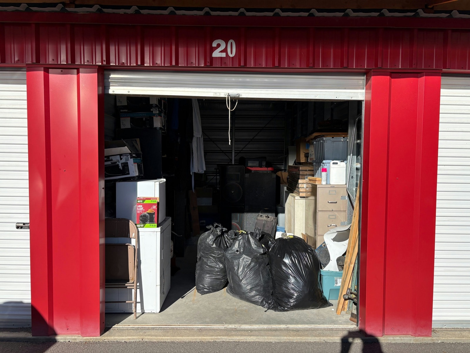 Open self-storage unit packed with appliances, boxes and garbage bags before a storage unit cleanout